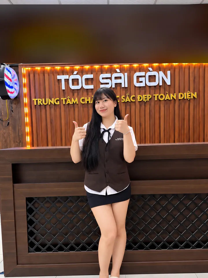 Nhật Lệ, kỹ thuật viên gội đầu, giơ hai ngón cái trước quầy lễ tân
