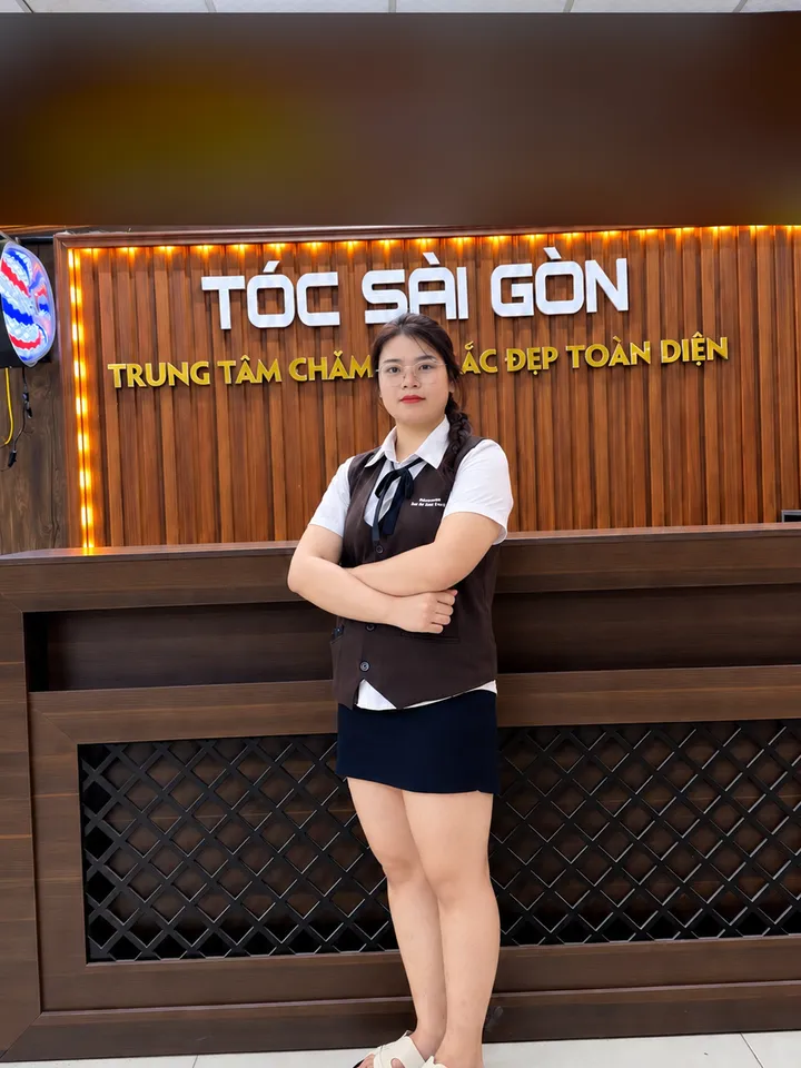 Quỳnh Quỳnh, kỹ thuật viên gội đầu, đứng khoanh tay trước quầy lễ tân