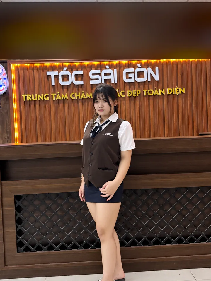 Vy, kỹ thuật viên gội đầu, đứng trước quầy lễ tân