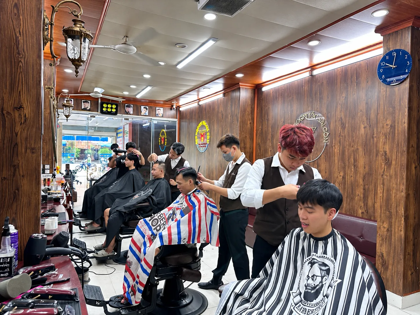 Khu cắt tóc tại TÓC SÀI GÒN: nhiều thợ đang làm việc, tường gỗ và ghế barber