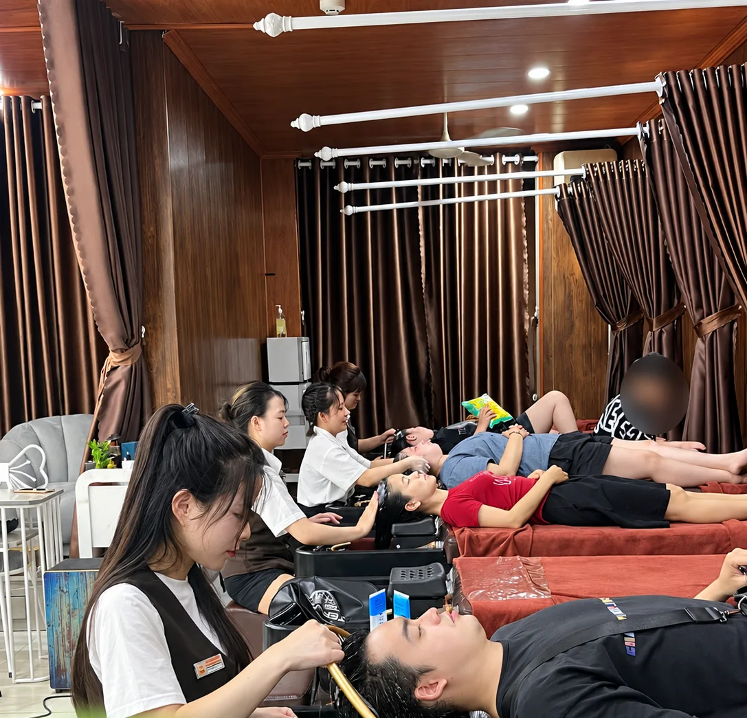Khu gội đầu với rèm nâu, kỹ thuật viên đang gội đầu cho khách